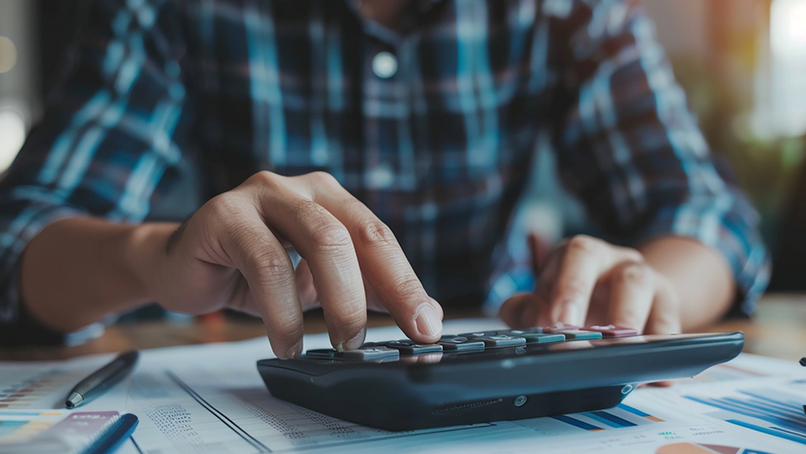 Osoba používa kalkulačku s finančnými dokumentmi.