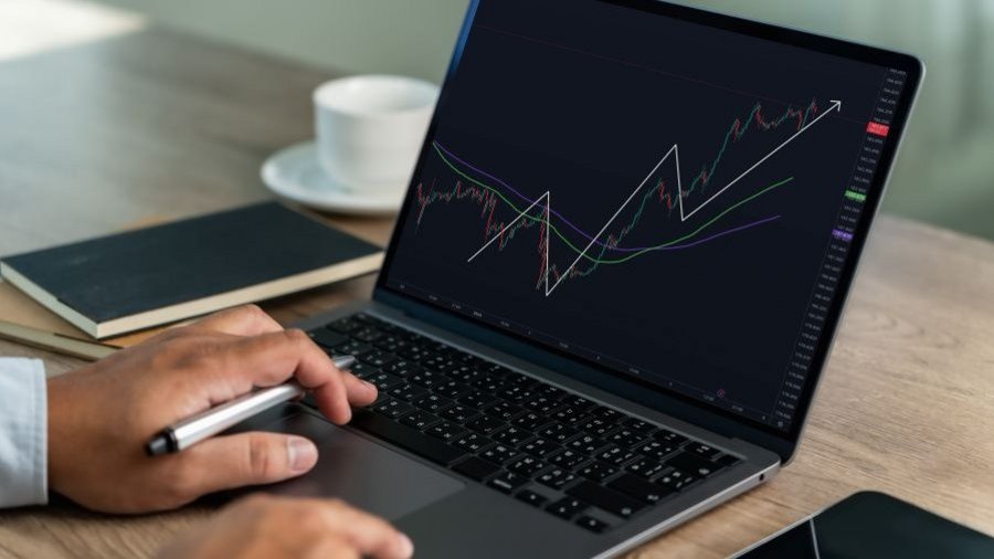 Osoba pracuje na notebooku so zobrazeným grafom vývoja finančných trhov a trendových línií.