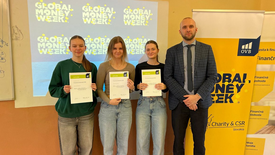Tri študentky s diplomami a lektor pózujú pred logom Global Money Week