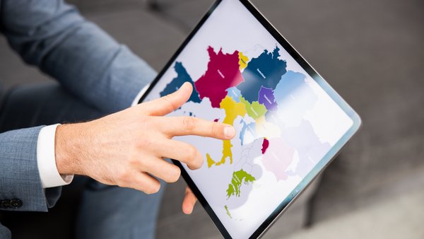 Osoba drží v rukách tablet, na ktorom je zobrazená mapa Európy, a ukazuje prstom na mapu Európy.