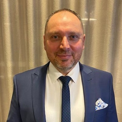 Muž v modrom obleku pred béžovým závesom