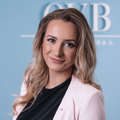 Žena v ružovom saku a čiernej blúzke pred modrým pozadím