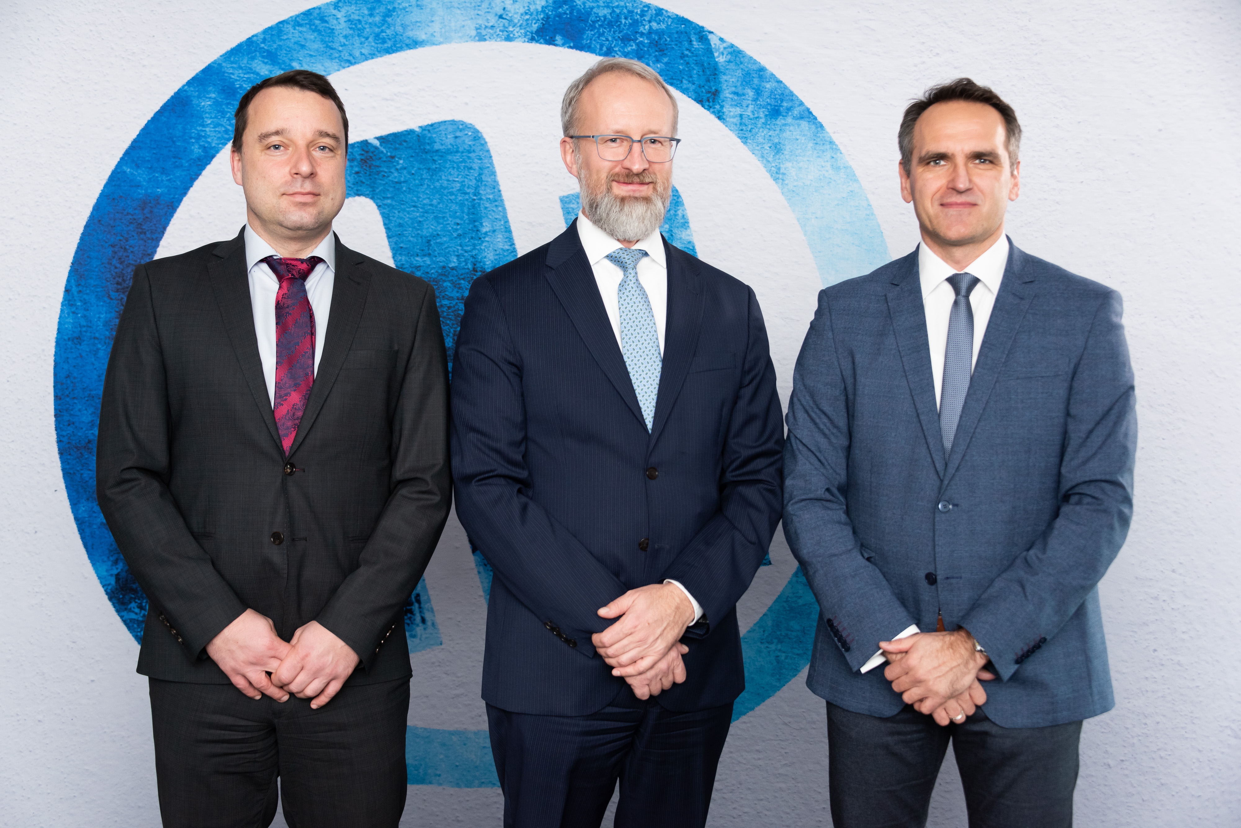 Traja muži v oblekoch pred logom spoločnosti