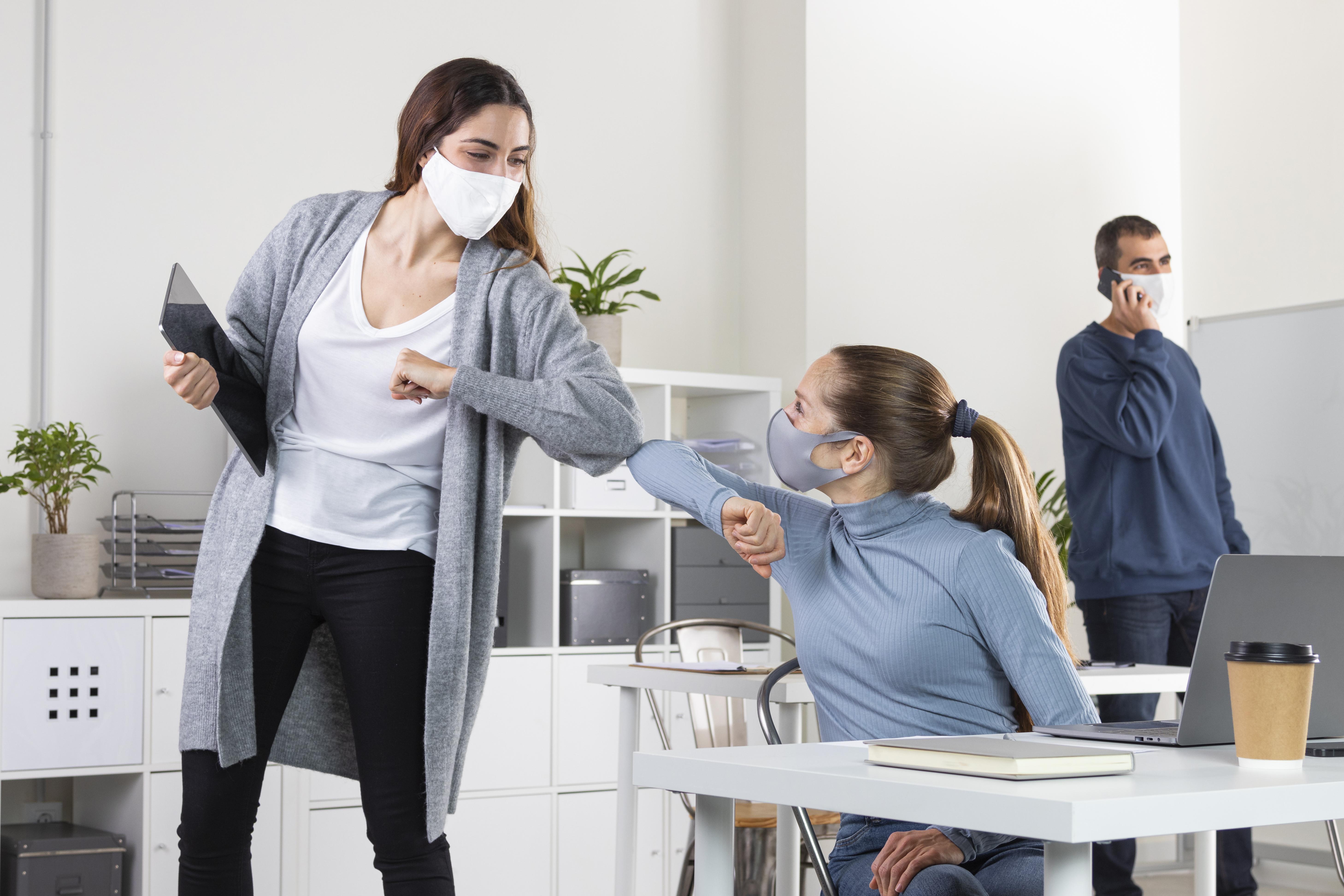 Zamestnankyne si dávajú lakťový pozdrav s rúškami