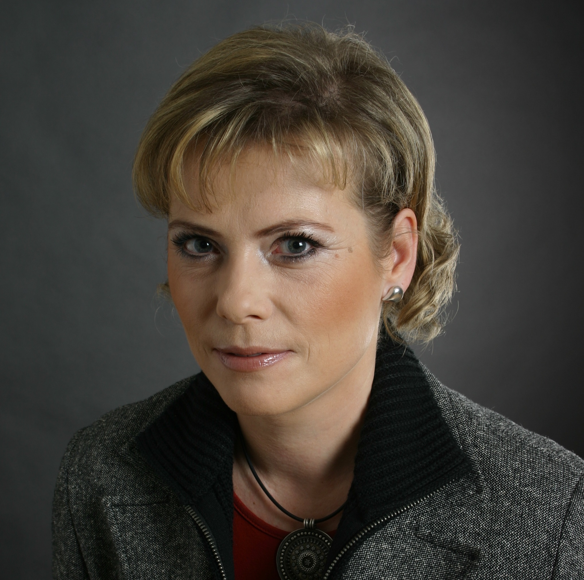 Žena v šedom saku pózuje pred tmavým pozadím