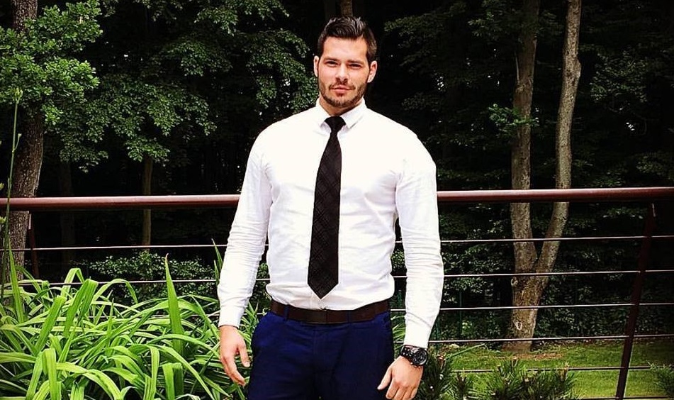 Muž v bielej košeli pózuje pred zeleňou