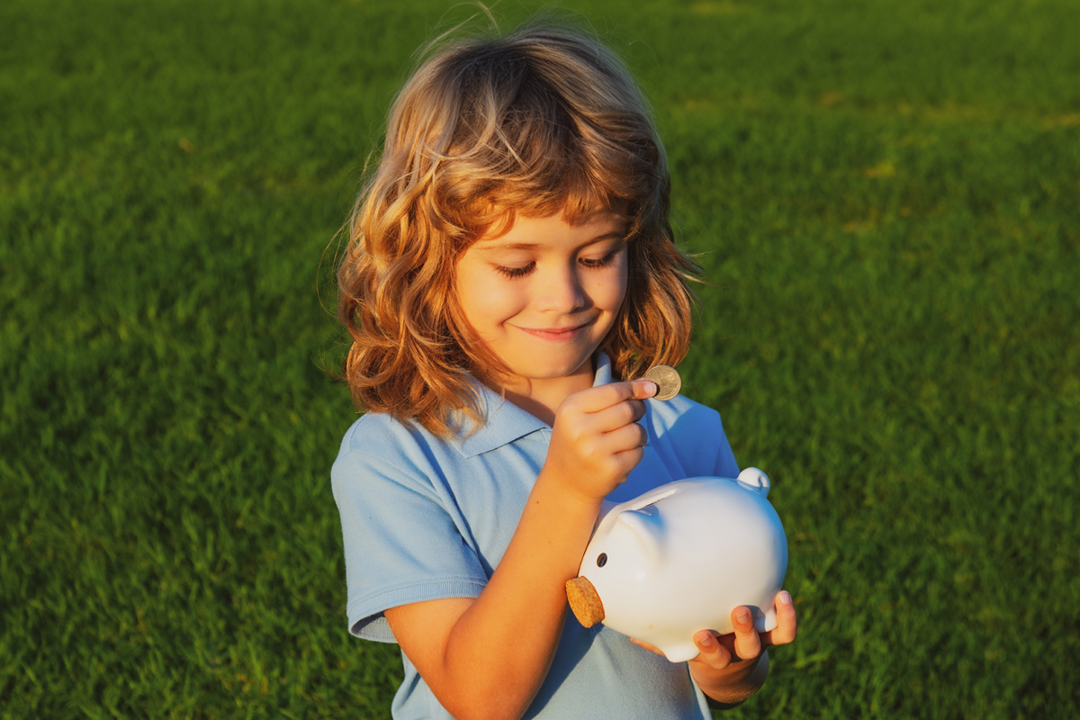 Usmievavé dievča v modrom tričku vkladá mincu do bielej pokladničky na lúke