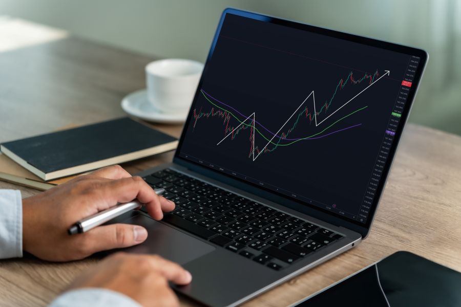 Osoba pracuje na notebooku so zobrazeným grafom vývoja finančných trhov a trendových línií.