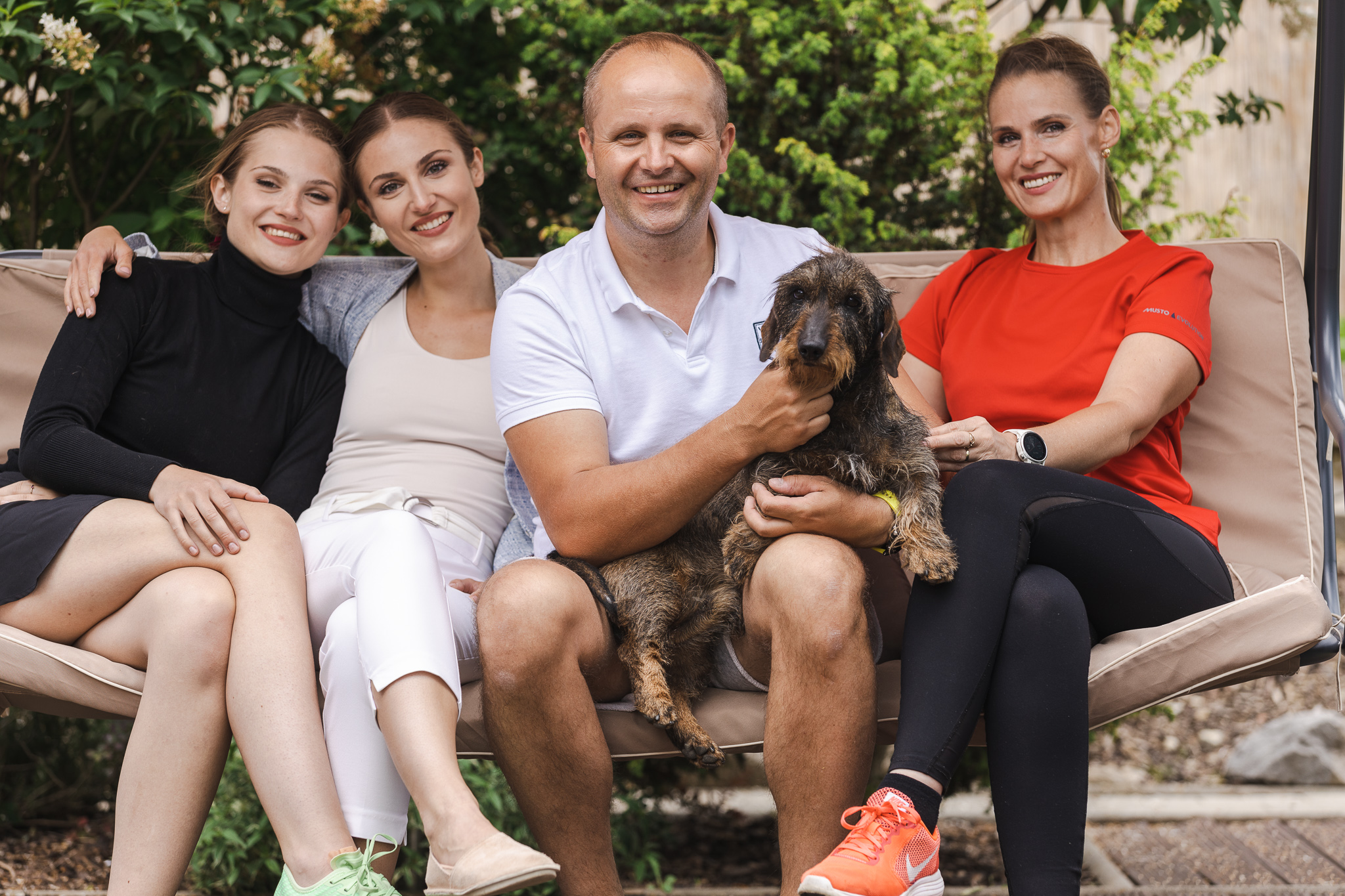 Rodinná fotografia štyroch ľudí sediacich na záhradnej hojdačke so psom