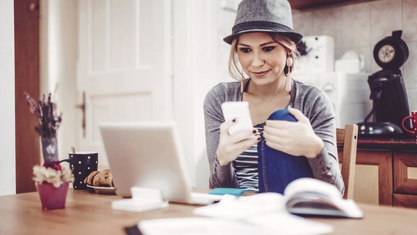 Mladá žena pri stole so smartfónom, notebookom a dokumentmi na vedenie knihy o rozpočte domácnosti