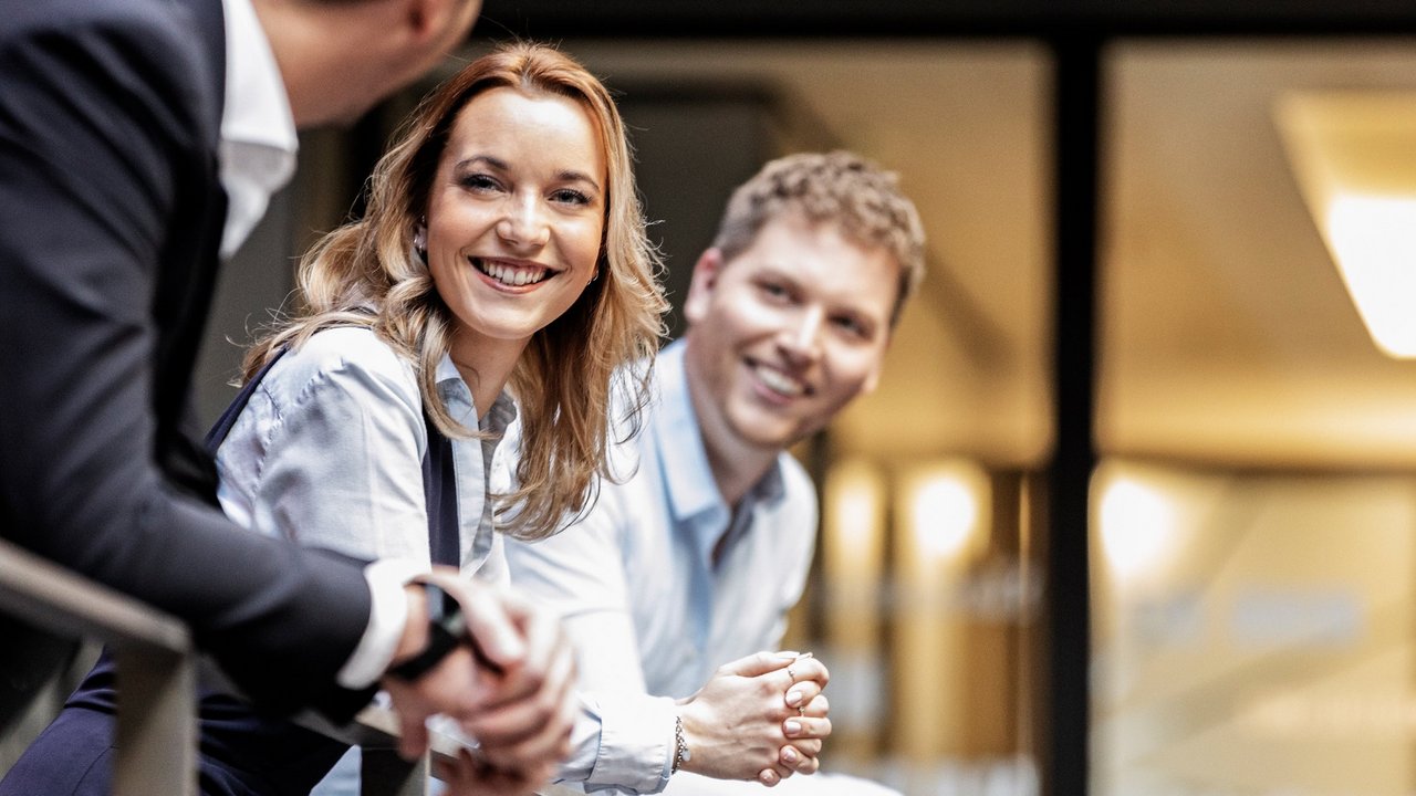 Niekoľko mladých ľudí v business oblečení sa rozpráva pri zábradlí v kancelárii.